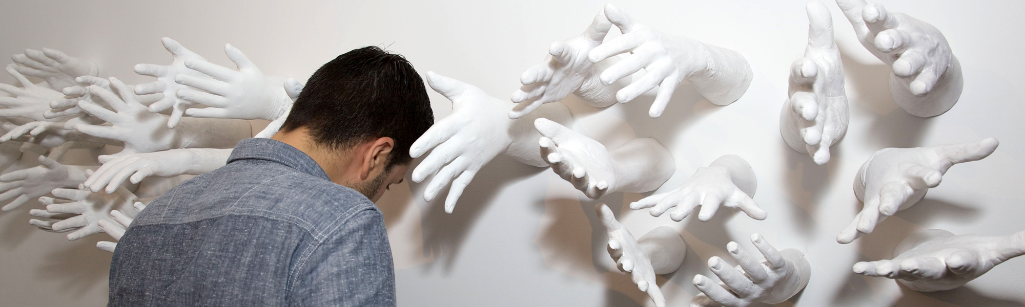 A wall sculpture having many hands and a person leaning towards them