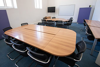 A lecture room with a large table and chairs and a monitor